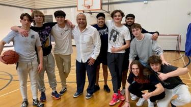 Group of students and Superintendent gather on basketball court after playing a game