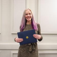 Female ABC award recipient stands in front of wall holding certificate