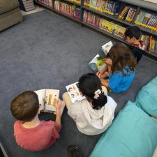 Four students sitting on carpet in library reading books